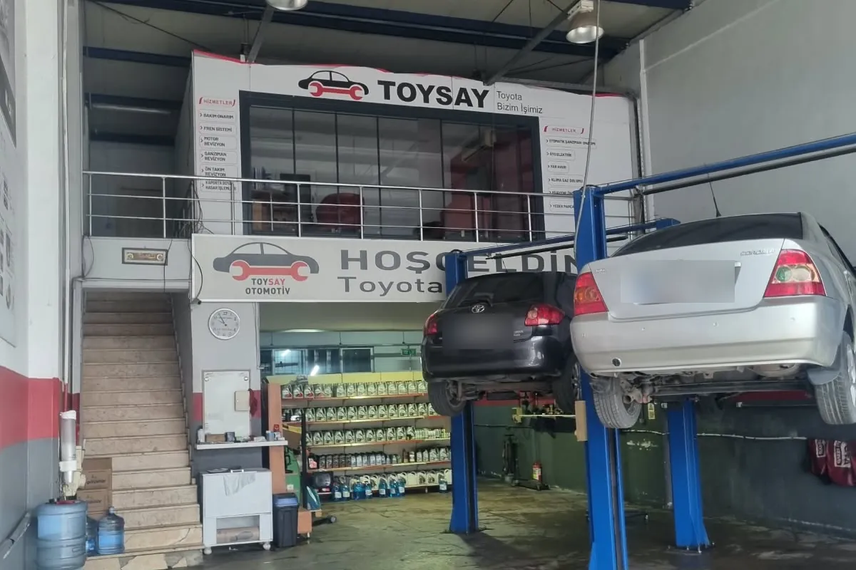Toysay atölyesinin içi: iki liftte bakımdaki Toyota araçlar, arkada Hoş geldiniz panosu